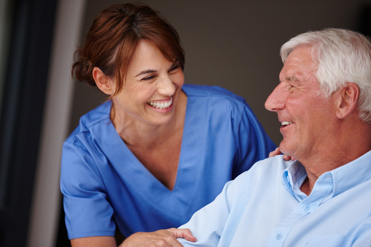 A woman in scrubs smiles with a seated eye surgery patient, a mature man smiling
